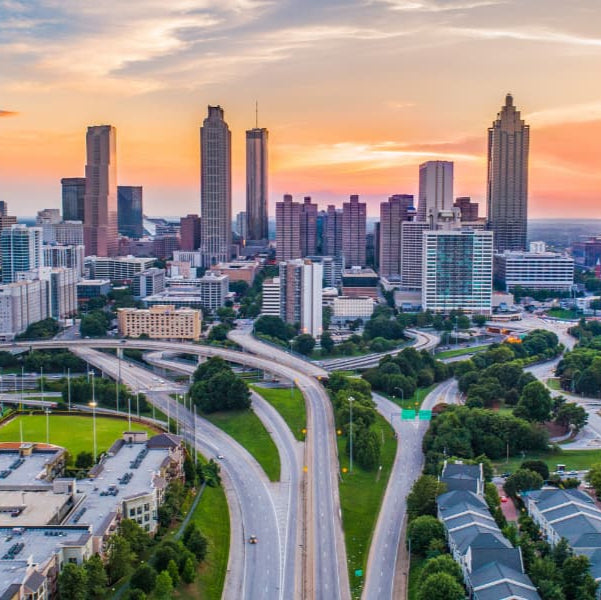 City skyline with tall buildings during sunset, featuring roads and green spaces.