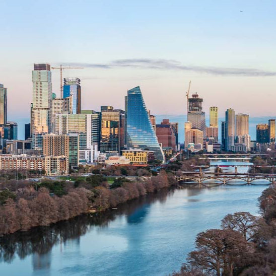 City skyline with modern buildings and a river, likely during sunset or sunrise.